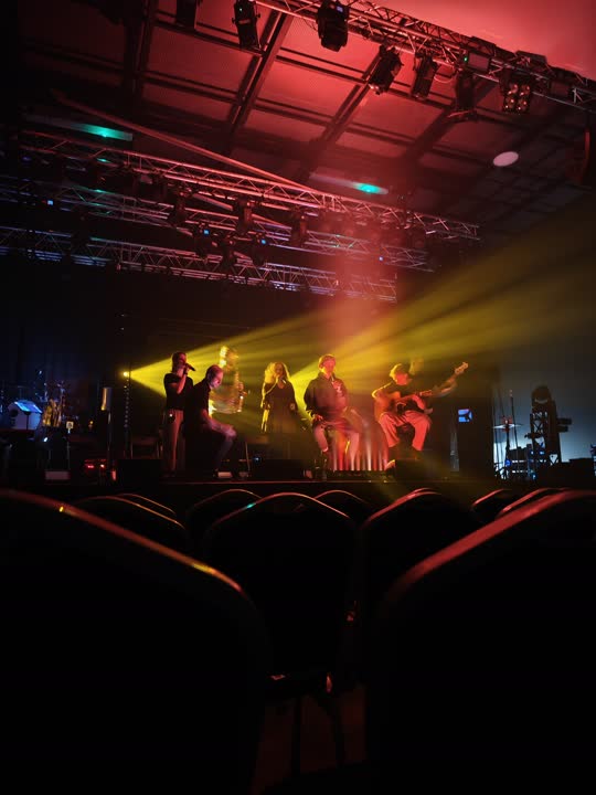 Koncertní stage s červeným nasvícením a hudebníky v živém vystoupení.