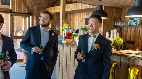 The groom and wedding guests holding glasses in a wooden interior.