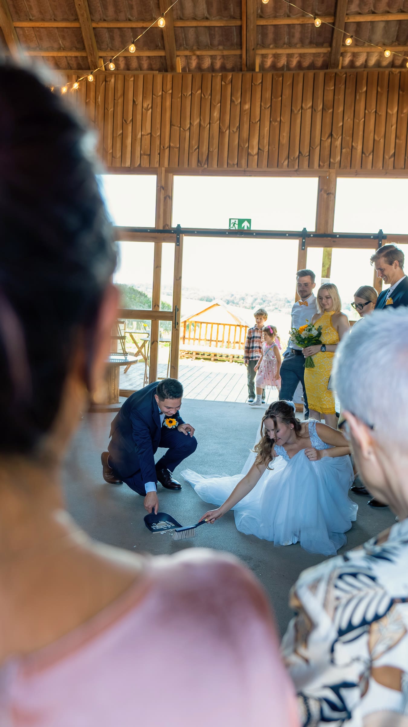 The newlyweds sweeping up broken crockery during a wedding tradition, photographed between guests.